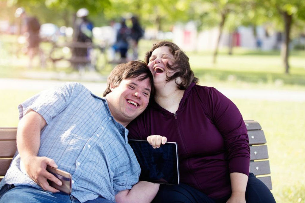 Couple in love of 26 years old Down Syndrome in a park in Montreal doing selfie with mobile phone. They are learning to live independently. Color and horizontal photo was taken in Quebec Canada.